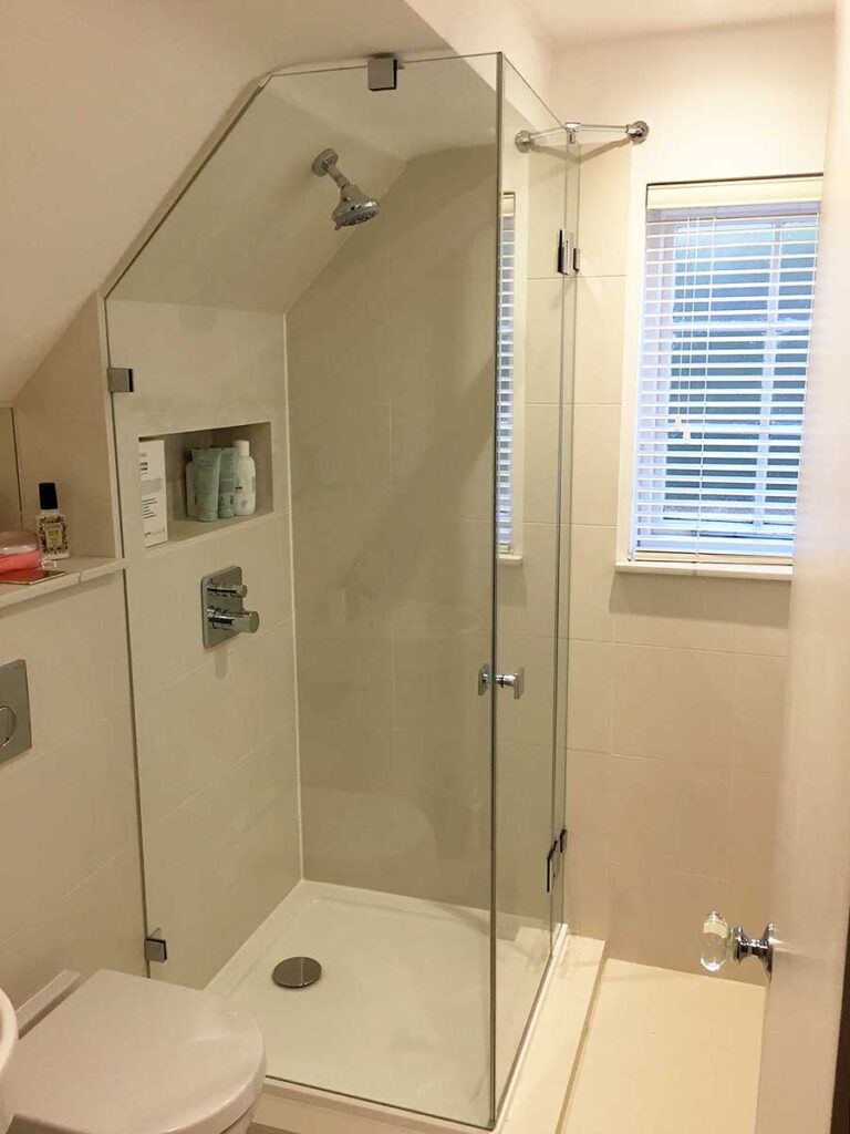 Small corner shower enclosure with glass shaped to fit the angle of a sloping ceiling